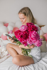 Image of a happy positive pretty young woman indoors at home  in bedroom in bed holding flowers take a selfie by mobile phone.