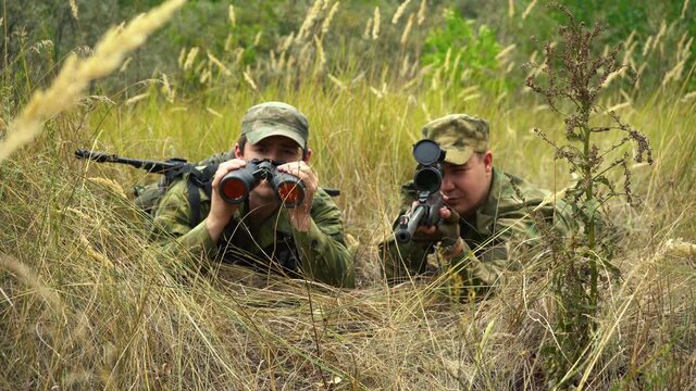 sniper with a gunner are sitting in ambush in the bushes