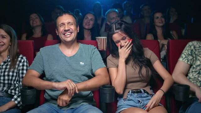Happy Hispanic couple laughing watching comedian movie at cinema sitting on armchair in row