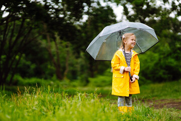 Little girl with transparent umbrella  playing in the rain on sunny autumn day. Beautiful girl  in a yellow cloak and rubber boots. Fall outdoor activity by rainy weather.