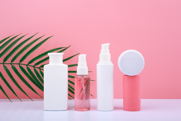 Trendy composition in pink colors with set of cosmetic bottles with beauty products against pink background with palm leaf. Concept of organic cosmetics for anti acne or anti aging treatment