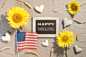 Happy Thanksgiving text on blackboard. USA flag, sunflowers, Autumn decorations. Flat lay on beige...