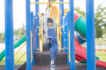 A little girl in casual clothes playing on kids playground, holding and climbing. Selective focus on girl's head.