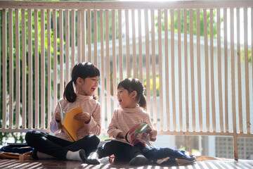 Cute Asian siblings girl reading a book at home. - obrazy, fototapety, plakaty