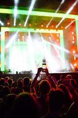 Using a smartphone in a public event,  live music festival.  Holding a mobile phone in hands and shooting photo or video content.  Youth, party, vacation concept.
