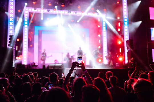 Using a smartphone in a public event,  live music festival.  Holding a mobile phone in hands and shooting photo or video content.  Youth, party, vacation concept.