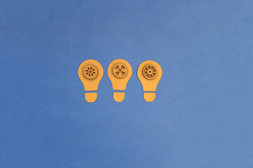 Electric light bulbs are yellow, inside there are wooden gears of blue color on a blue background. Ideas, creativity.