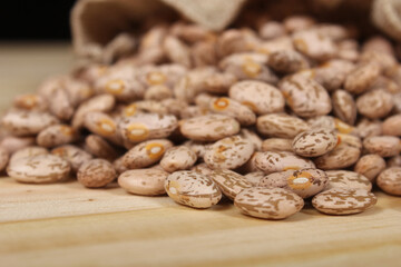 Burlap Bag of Dried Pinto Beans Spilled on Wooden Table