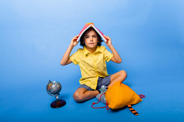 Cute baby with a book on his head. A schoolboy with a book on his head sits on the floor....
