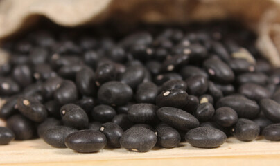 Fototapeta na wymiar Burlap Bag of Dried Black Beans Spilled on Wooden Table