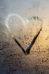 symbol of beautiful heart with the yellow sunlight painted on misted glass, texture of frost and water drops, empty space for an inscription. vertical frame out of focus