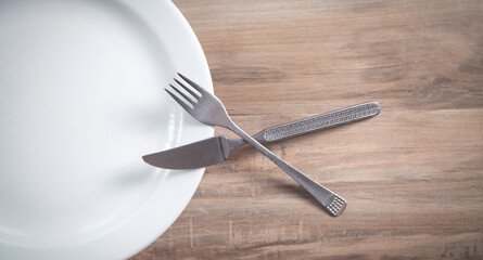 Empty plate with fork and knife on wooden table.