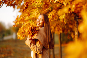 Young woman having fun throwing leaves in autumn at city park. Lifestyle. Relax, nature concept. Autumn mood concept.