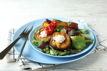 Plate of salad with grilled peach on white wooden table