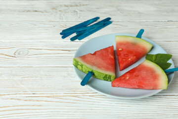 Ice sticks with watermelon slices on plate on white wooden table