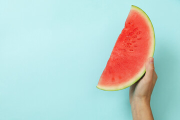 Fototapeta na wymiar Female hand holds watermelon slice on blue background