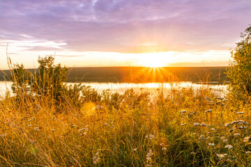 Scenic view at beautiful sunset or sunrise on a shiny lake with bright grass on the foreground, trees, golden sun rays, calm water ,nice cloudy sky on a background, spring landscape