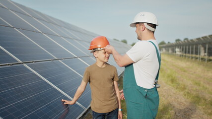 An young engineer father is explaining to his little son an operation and performance of photovoltaic solar panels at sunset. Concept: renewable energy, technology, electricity, green, future, family.