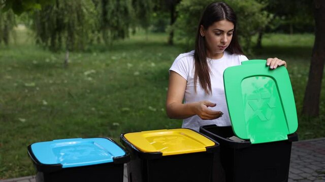Female hold rubbish, egg carton and thowing into recycling bin. Close-up of woman stand by blue, yeallow and green bin