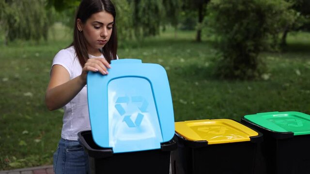 Middle selection of female hold two different type of rubbish, glass bottle and plastic container and thowing into different recycling bins. Close-up of woman stand by blue, yeallow and green bin