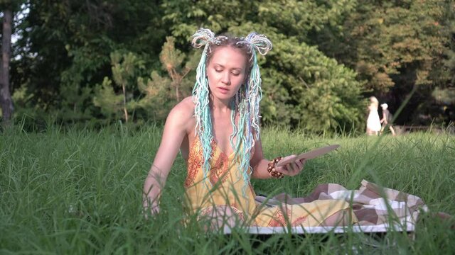 Young attractive woman artist with colored hair draws nature in the park