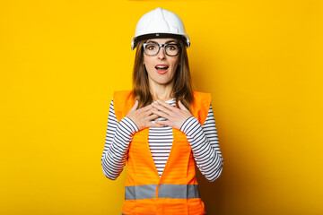 Young woman with a surprised face in a vest and hard hat on a yellow background. Construction concept, new building. Banner