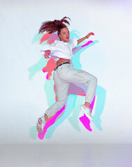 Jumping mixed race young girl dance in colourful light. Female dancer performer jump dancing fiery...