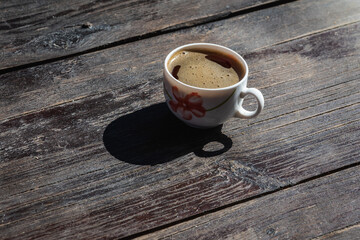 Cup of coffee in a white cup and a metal teaspoon on a gray-cinnamon wooden surface, light shadow,...