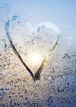 symbol of beautiful heart with the sun inside painted on misted glass, moonlight, texture of frost and water drops, empty space for an inscription. vertical frame out of focus