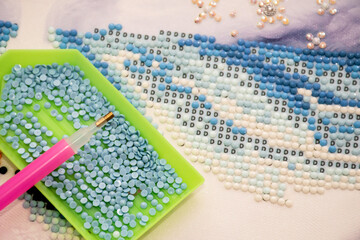 Diamond painting embroidery craft. Acrylic rhinestones and pen tool. Closeup, selective focus.