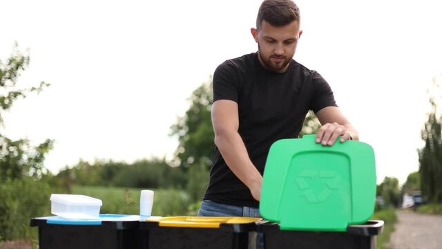 Handsome man put garbage into recycling bins outddors. Concept of recycling. Tree bins, green, yeallow and blue. Lady put different kind of rabbish in trash container