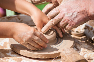 Pottery training - male hands and children make a clay jug on a potter's wheel, close-up