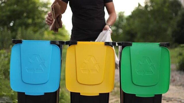 Middle secection of young man taking from eco packager garbage and put them into recycling bins outddors. Concept of recycling. Tree bins, green, yeallow and blue. Lady put different kind of rabbish