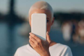 Short haired woman covering close face with smartphone. Mobile phone data security, privacy and...