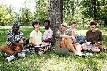Group of people sitting on the grass and looking at camera they meeting in the park at seminar