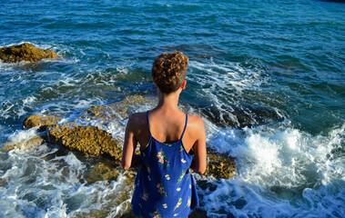 Fototapeta premium Beautiful young woman in a dress sitting by the sea in Spain.