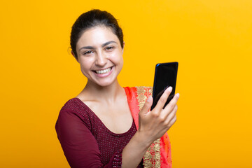 Portrait of positive smiling young adult indian woman in sari having video call with mobile phone look camera