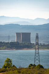 Fototapeta premium Two refrigeration towers from a power station next to a lake with some mountains on the background