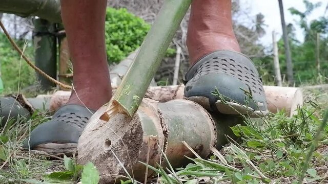 A man chops bamboo with a machete. They build a house.