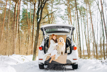 Young woman and cute golden retriever dog sitting in the trunk of a car winter season, traveling.