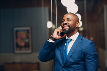 Portrait smiling african american businessman in blue suit in office with mobile phone speaking...