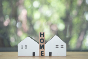 Text of HOME on wooden block in middle of two miniature wood home.