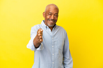 Cuban Senior isolated on yellow background shaking hands for closing a good deal