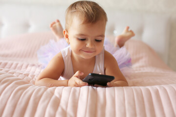 a little happy beautiful girl is lying on a pink blanket in a skirt and holding a phone in her hands