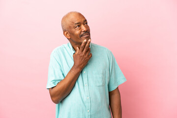 Cuban senior isolated on pink background looking up while smiling