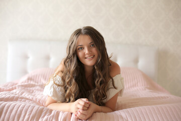 a young beautiful girl in x with dark long hair in a white dress lies on a pastel on a pink blanket and a pillow