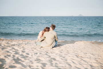 Fototapeta na wymiar Lovely young couple sitting on the beach and cuddling and looking at the sea. Back side view. Honeymoon. Holidays. High quality photo