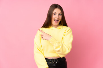 Teenager caucasian girl isolated on pink background surprised and pointing side