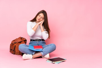 Teenager caucasian student girl sitting on the floor isolated on pink background making sleep gesture in dorable expression