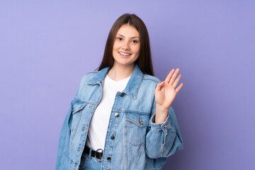 Teenager caucasian girl isolated on purple background saluting with hand with happy expression